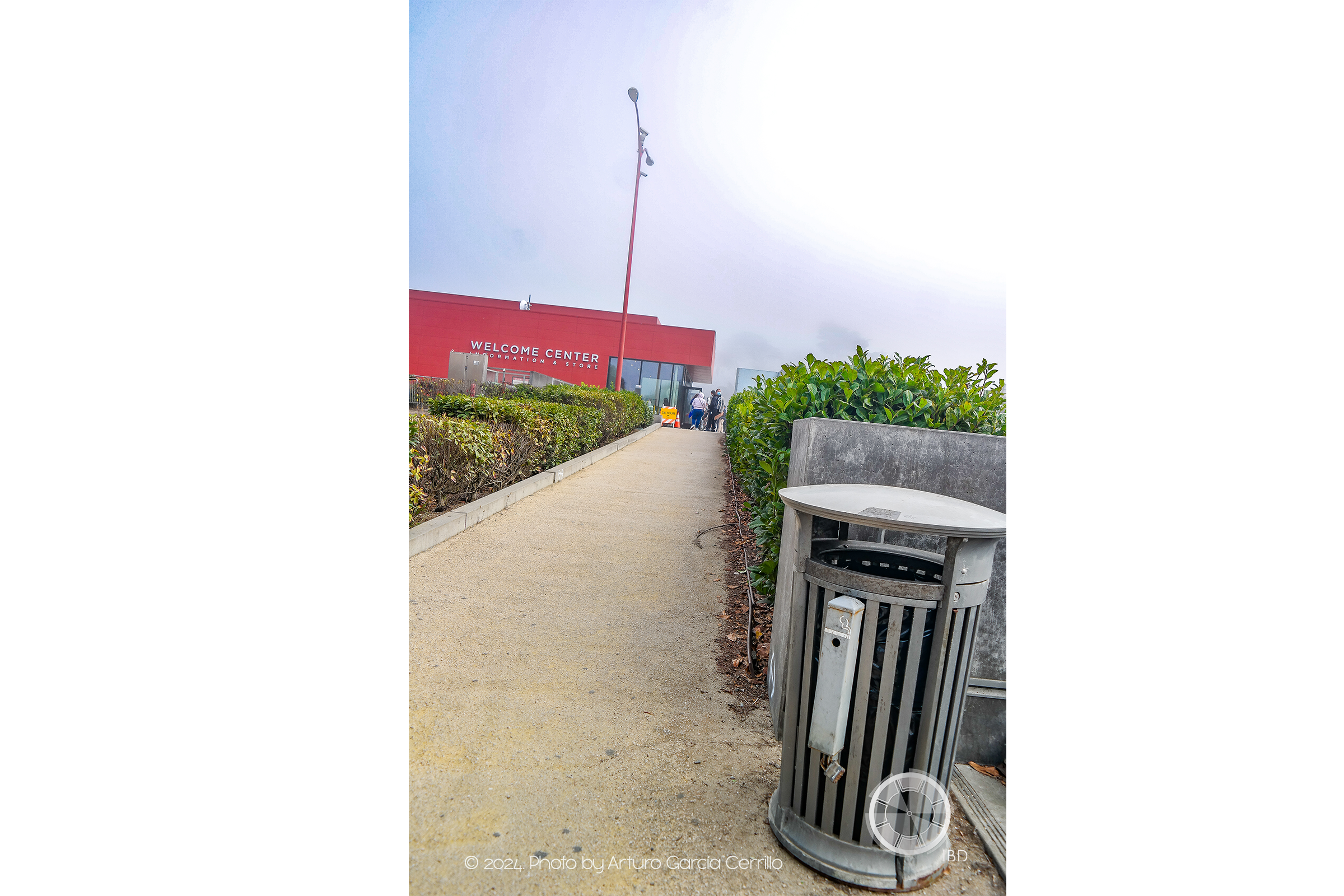 Vertical picture at hazy park. Dirt trail shown towards red building.