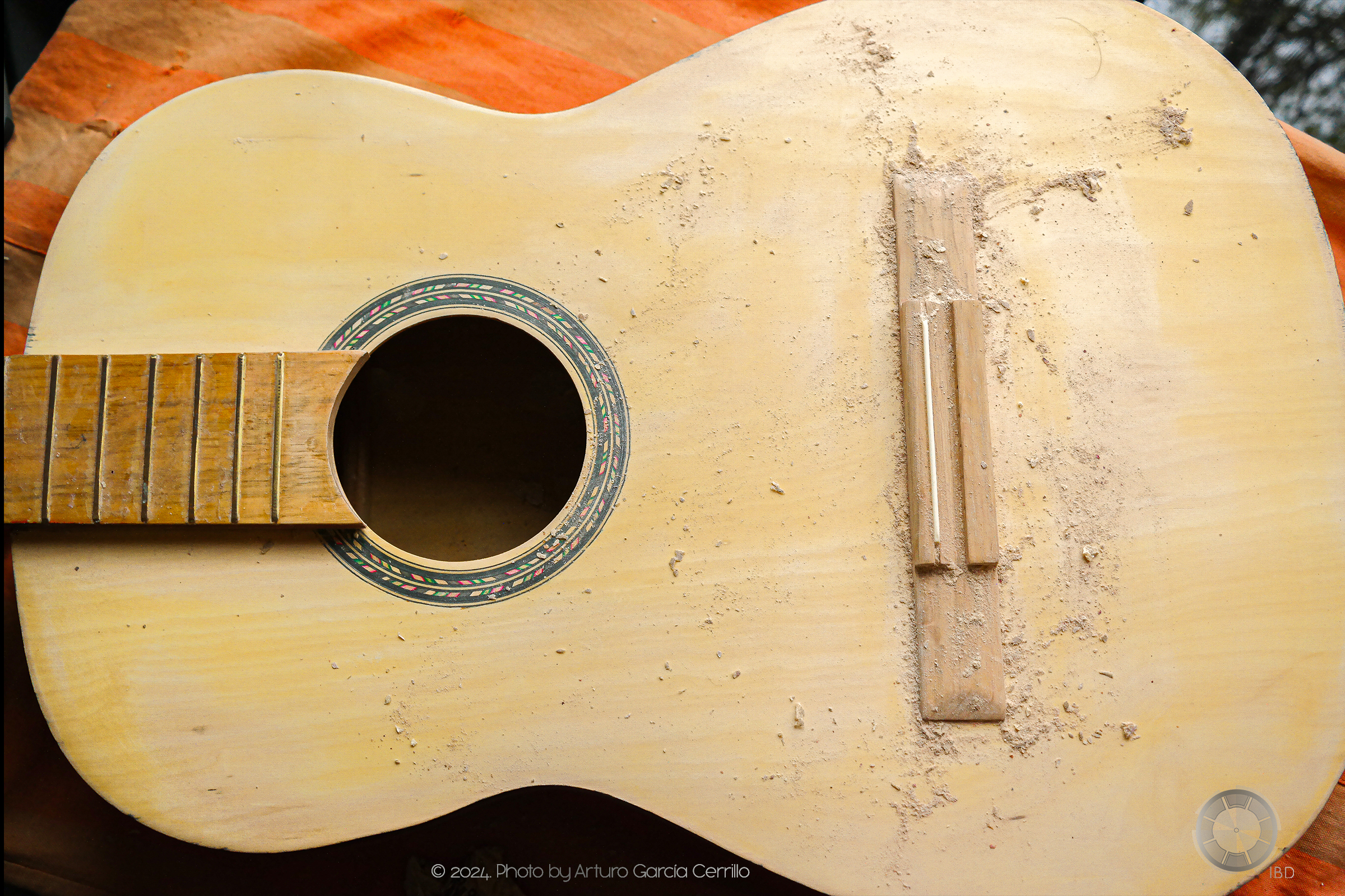 Picture from top of yellow acoustic guitar without strings. Residues of enamel resulting from sanding are shown.