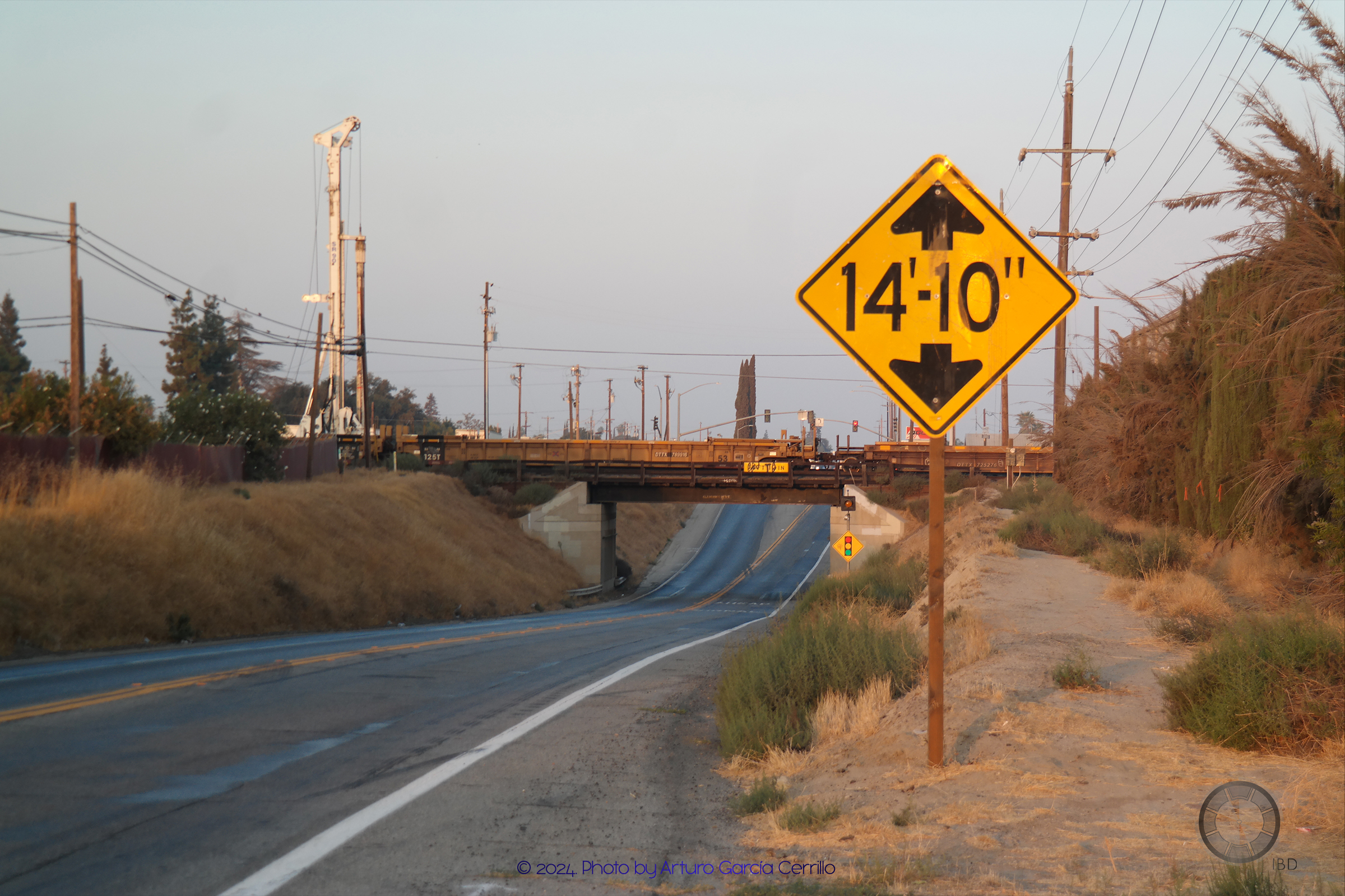 Picture of a dry grassy landscape with a road in the middle and a small bridge in the background