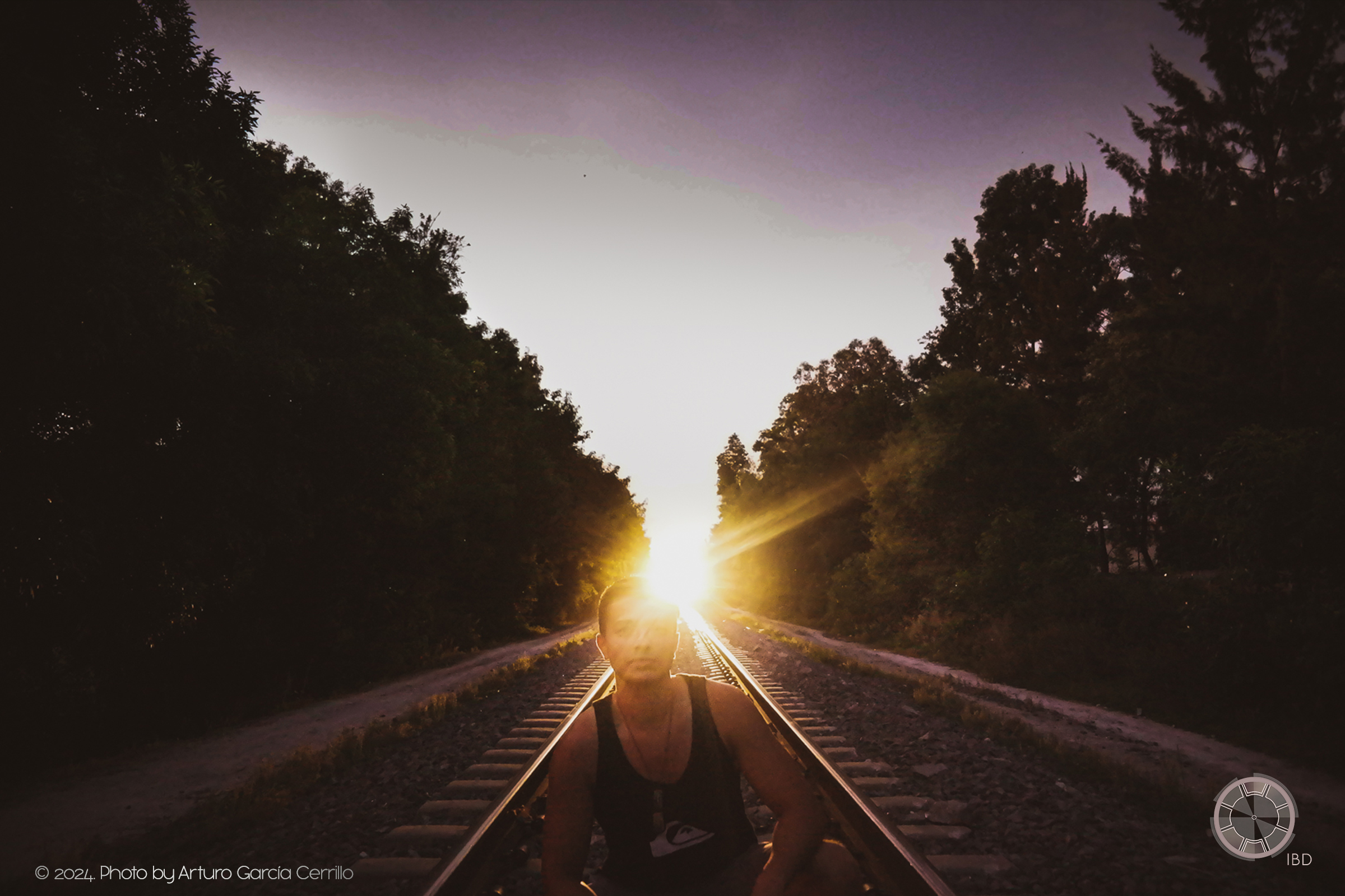 Portrait of guy crouching at the train tracks with train light behind