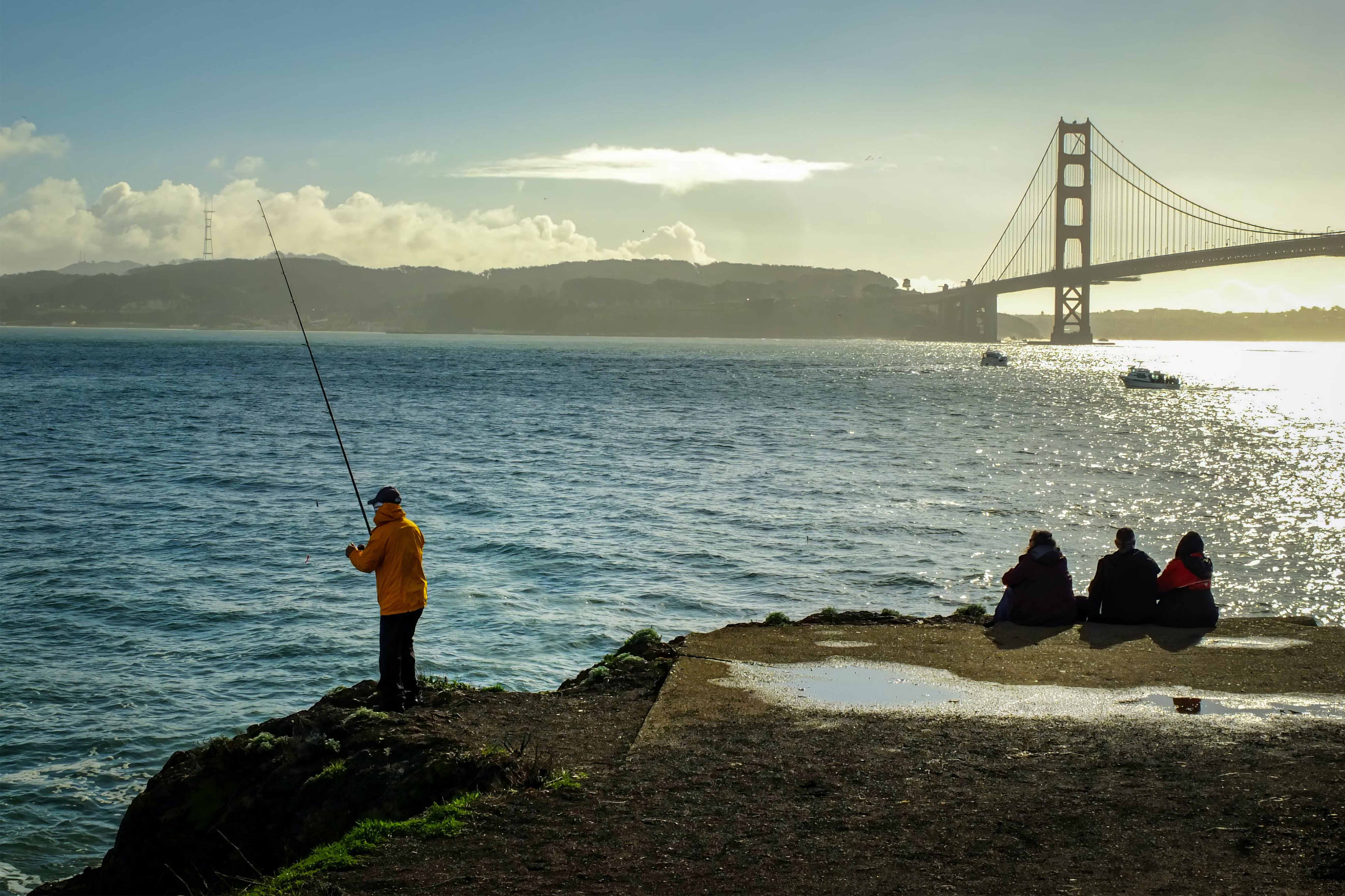 Picture of man fishing in ocean with bridge in the background