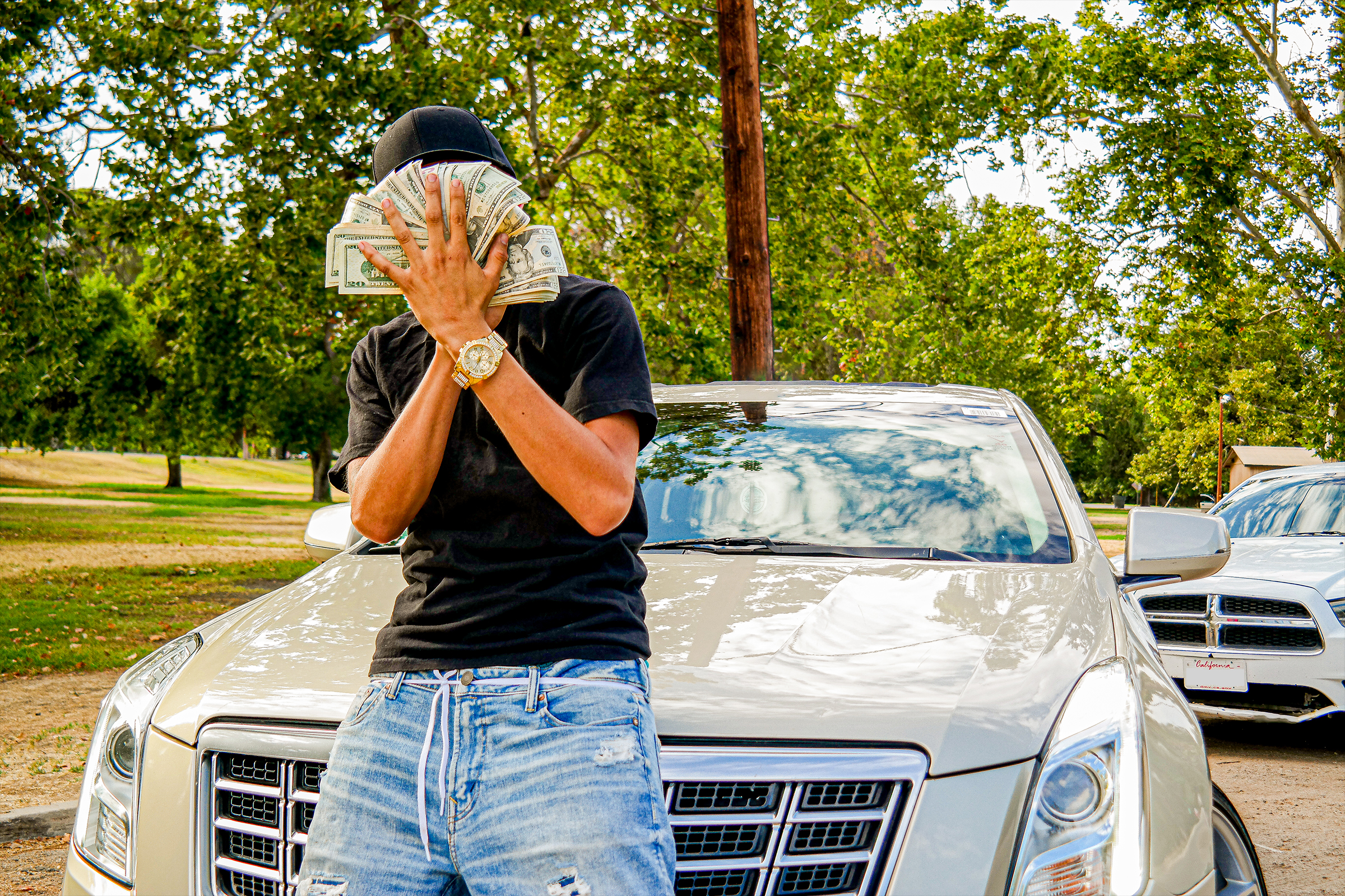 Portrait of guy holding bills in hand while laying on his golden Cadillac